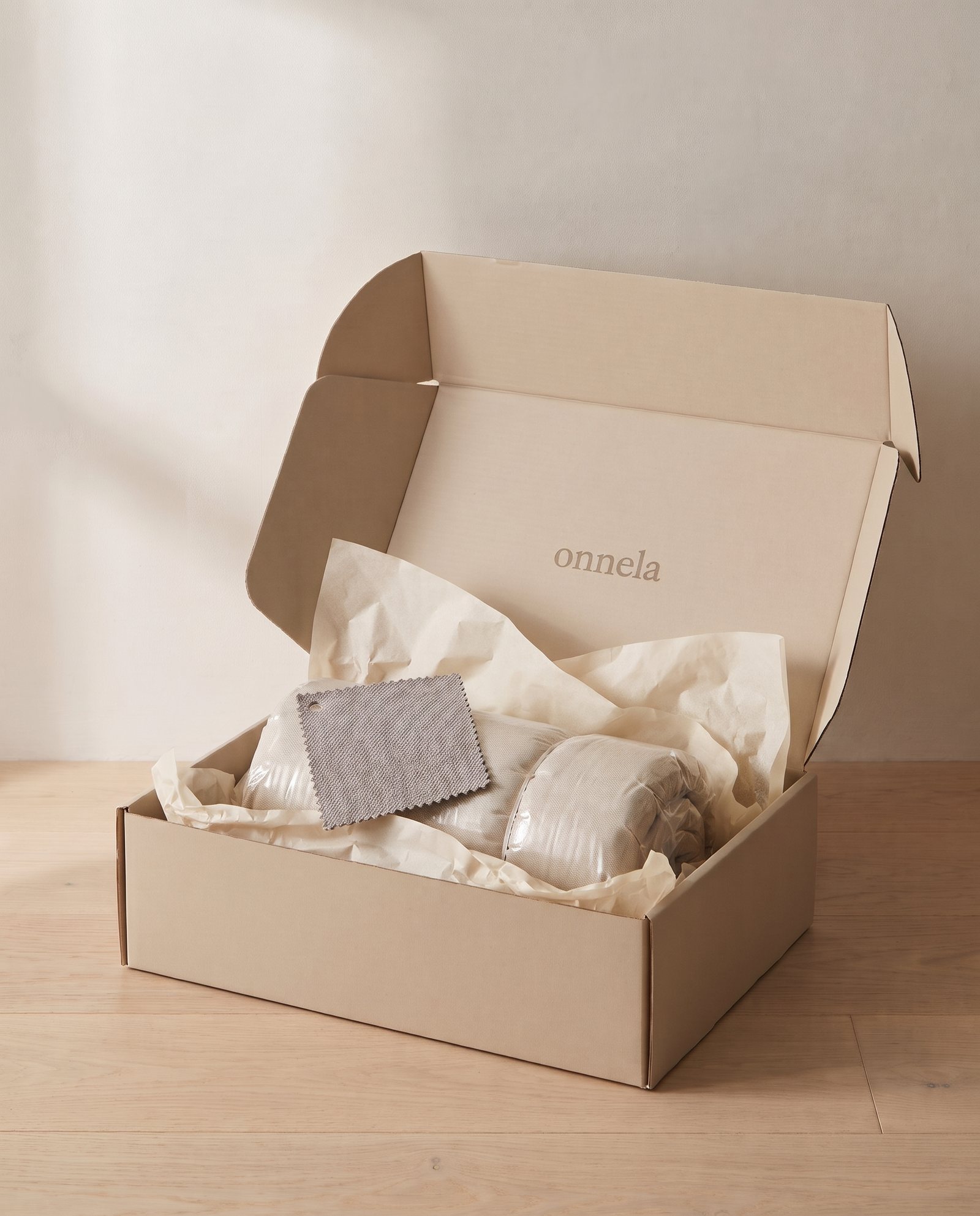 An opened kraft box with onnela printed inside the lid, tissue paper and a fabric swatch